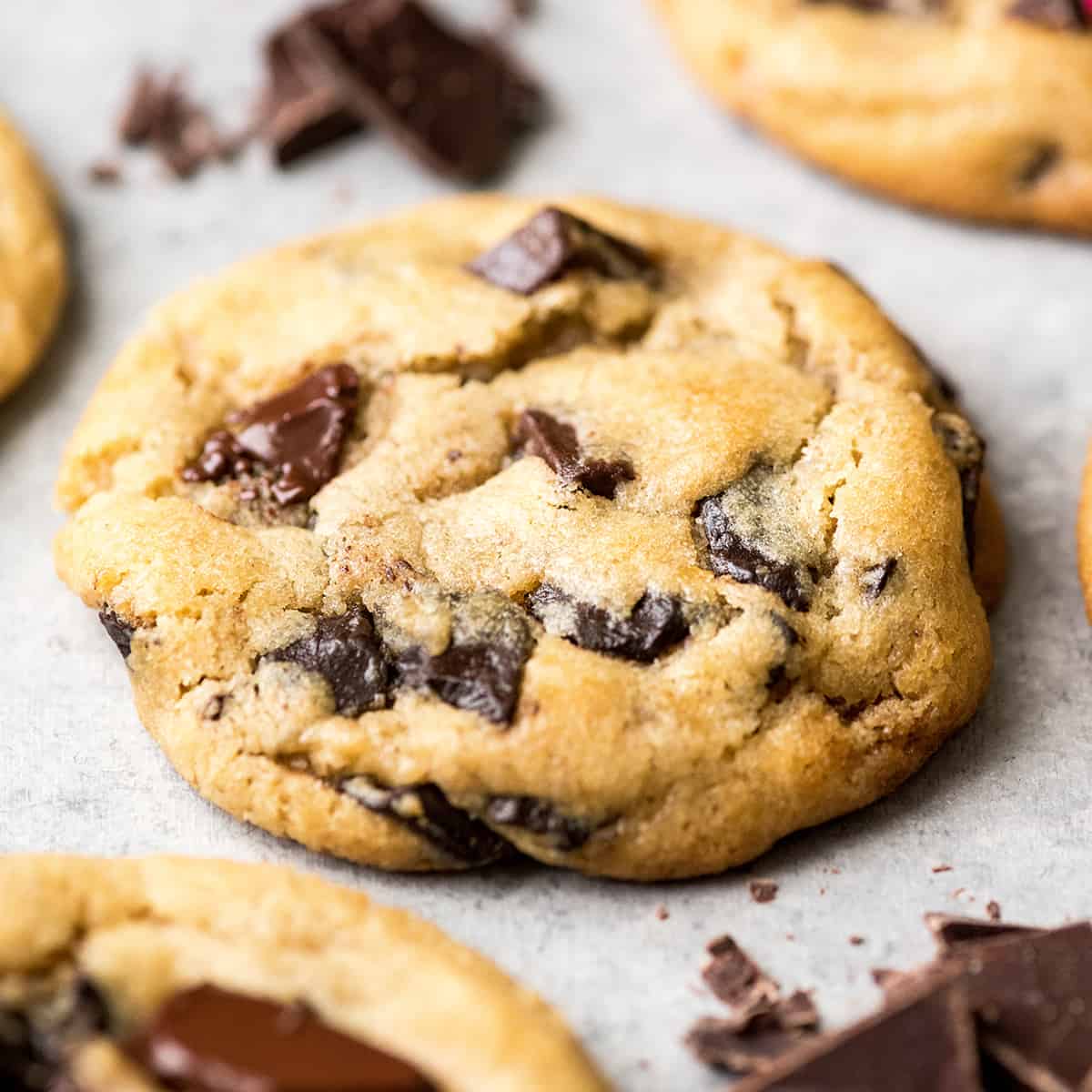 side view of the best chocolate chip cookie recipe ever one cookie with melty chocolate chips surrounded by three other cookies and chopped chocolate