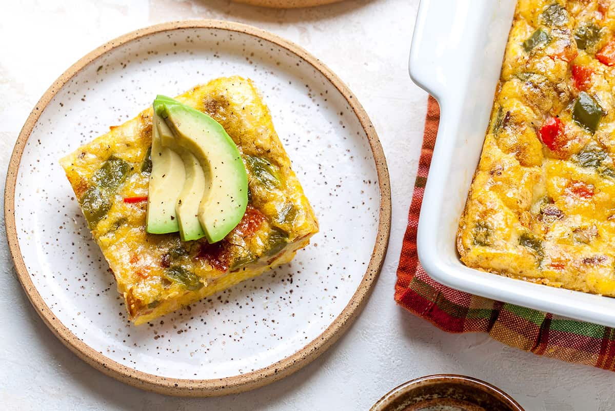 overhead view of a slice of egg casserole next to the baking dish of egg bake
