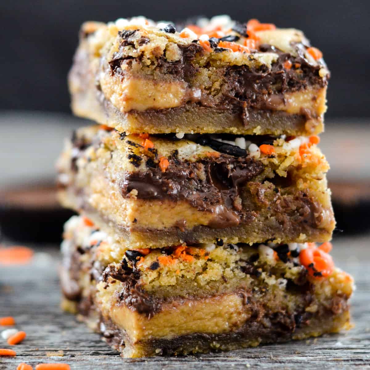 Candy Cookie Bars! Two layers of gooey chocolate chip cookie dough stuffed with the candy of your choice! The perfect dessert recipe to use up that Halloween Candy or adapt them for any holiday! #cookiebars #candycookiebars #chocolatechipcookiebars #cookies #chocolatechipcookies #dessert #recipe Front view of a stack of 3 Candy Cookie Bars.